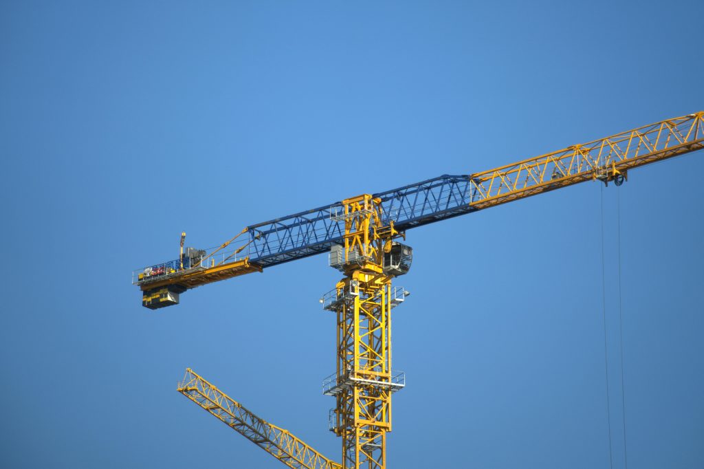 Close-up of a yellow tower crane with a clear blue sky background.